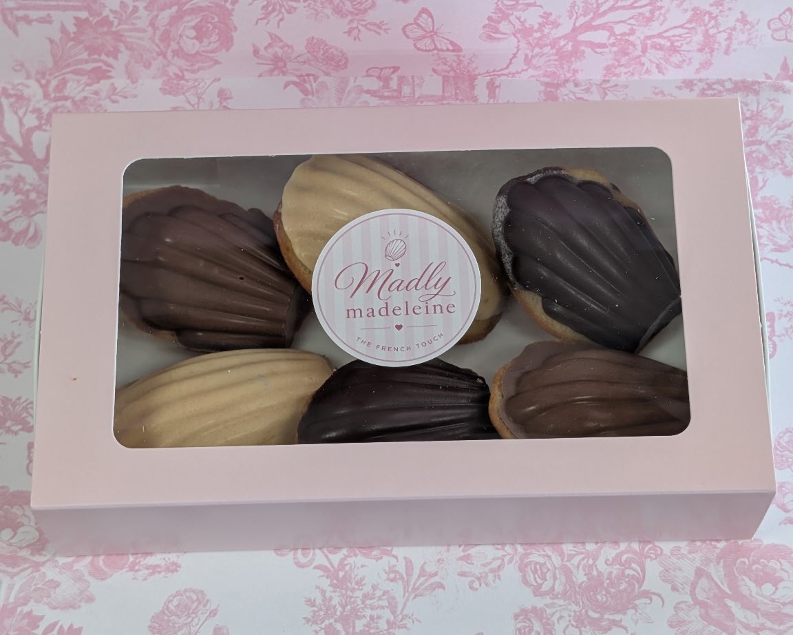 A pink Madly Madeleine box of six chocolate-dipped madeleines with the logo sticker