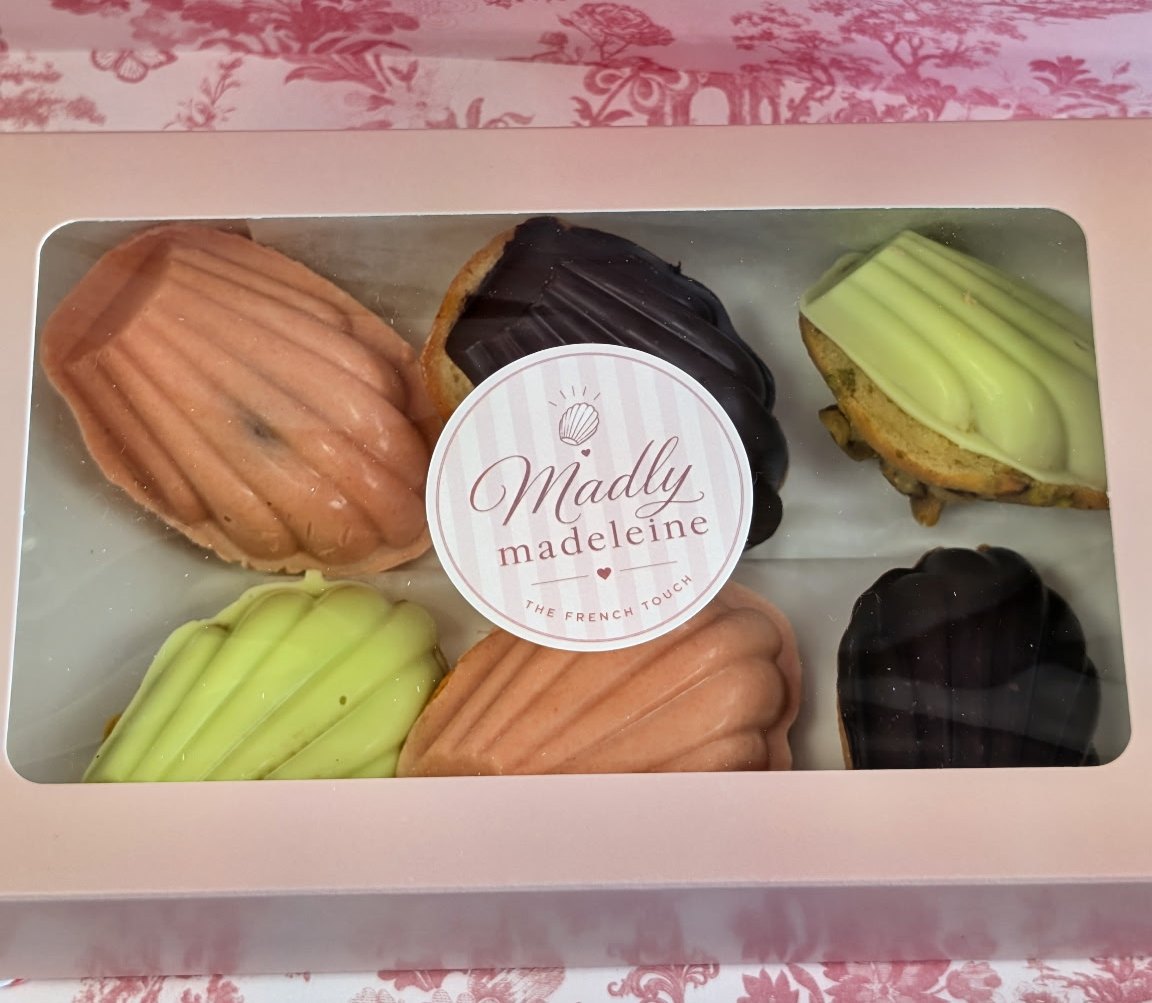 A pink Madly Madeleine box of six madeleines in peach, green and dark chocolate on pink floral paper