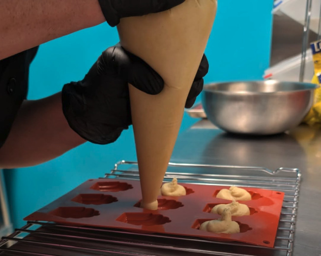 A gloved hand piping madeleine batter into a shell-shaped mold